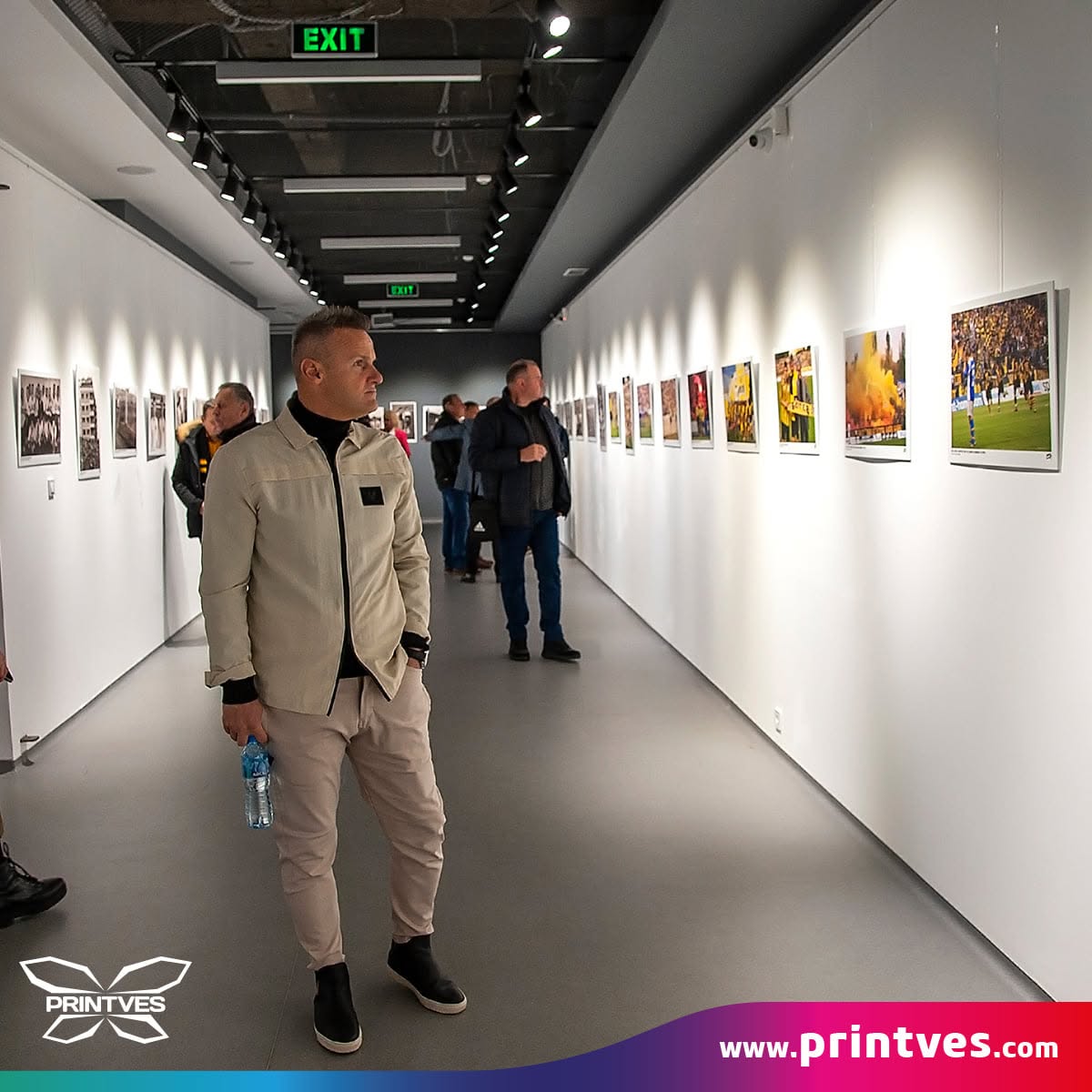 Мъж разглежда фотоизложба в дълъг бял галериен коридор